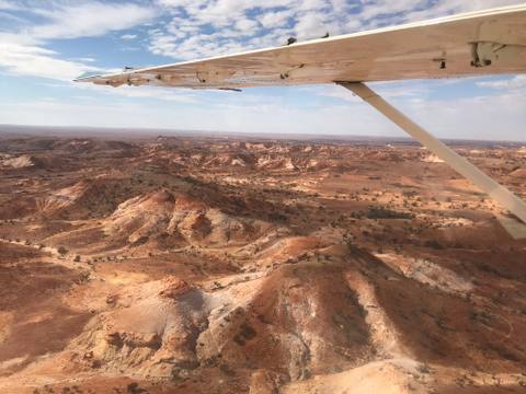Eroded red desert formations seen beneath an airplane wing