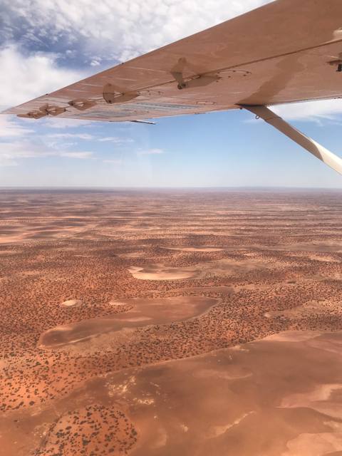 Red desert terrain seen beneath the wing of a survey airplane