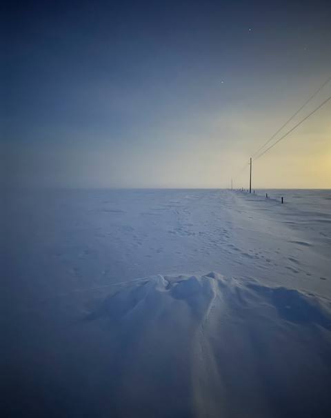 Windswept snowfield with utility poles on the horizon