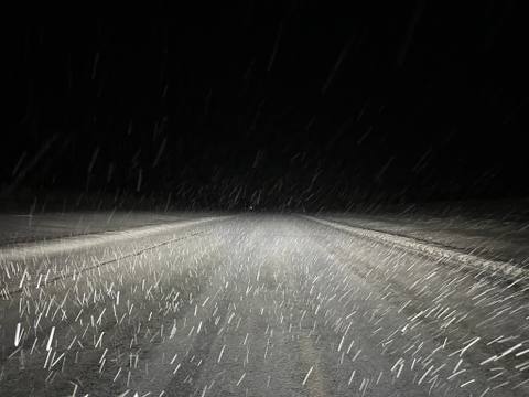 Snow streaking through headlights over a winter road