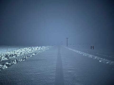 Icy road and utility poles receding into dense fog