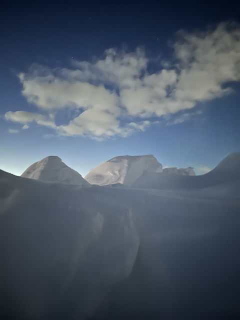 Snowdrifts and mountain silhouettes under broken clouds